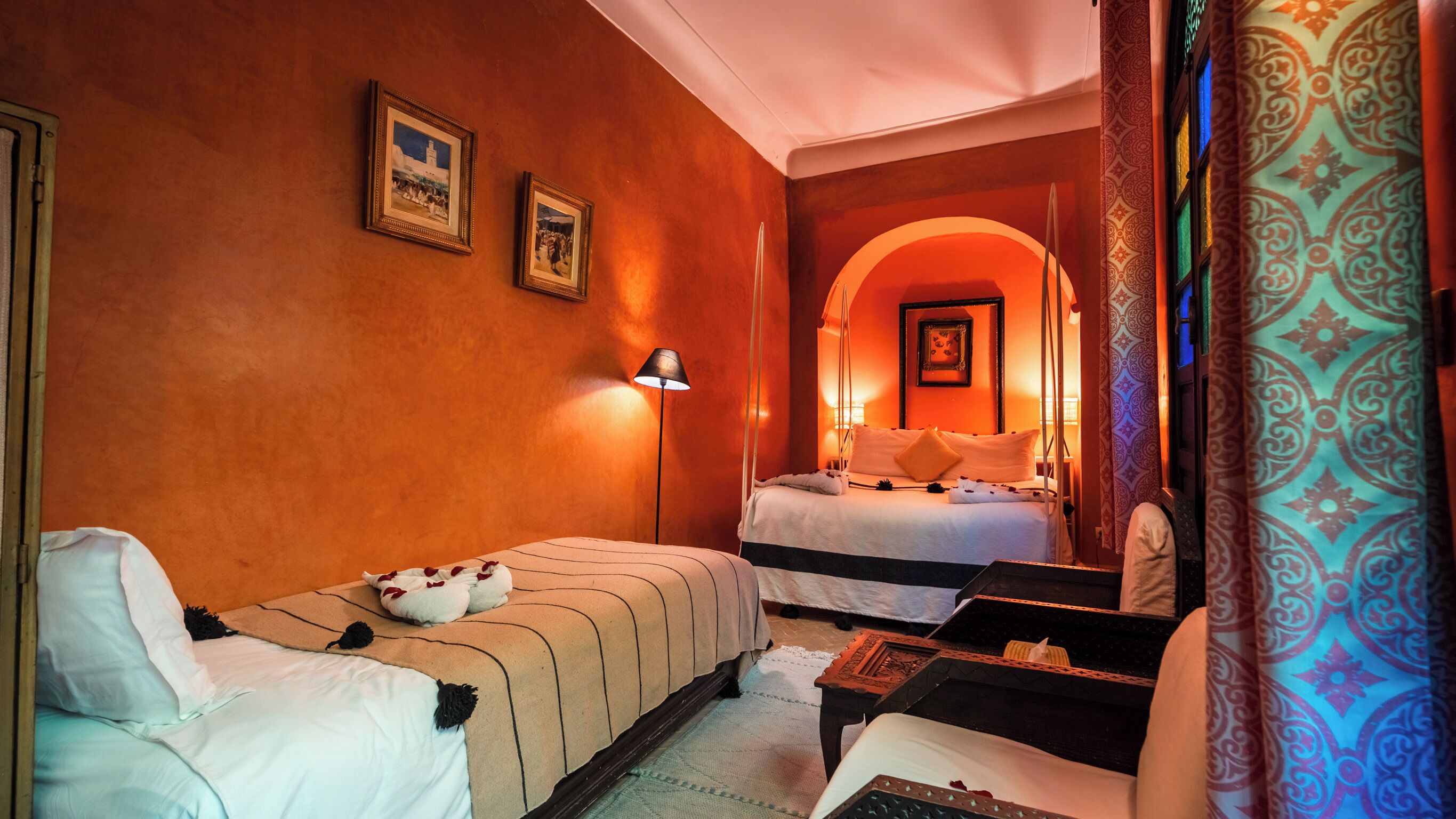 A hotel room with two beds, a sitting area, a lamp, and a patterned curtain.