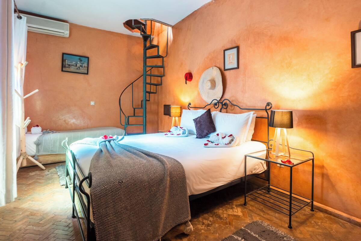 A bedroom with a bed, a nightstand, a lamp, a hat on the wall, and a picture.