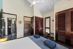 A hotel room with a large bed, wooden doors, a ceiling fan, and a bathroom with a shower and toilet. - A beautiful villa near the beach, with a beautiful view (Willemstad)