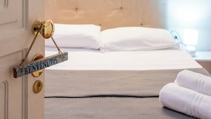 A hotel room with a bed, a bedside table, a lamp, and a door with a sign. - Yenne Home (Cagliari)