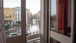A street view from a window with a view of buildings, a crosswalk, and cars. - Yenne Home (Cagliari)