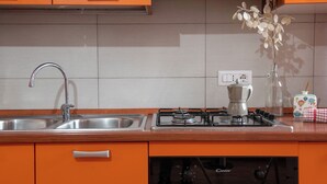 A kitchen with orange cabinets, a stainless steel sink, a gas stove, and a coffee maker. - Yenne Home (Cagliari)