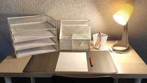 Een bureau met een lamp, een witte stoel, een zwart bureaublad en opbergdozen.