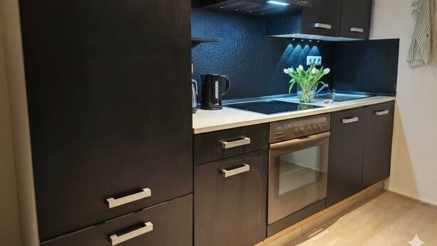 Een moderne keuken met donkere kastjes, een roestvrijstalen oven en een zwart aanrecht.