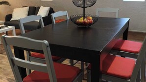 Een eetgedeelte met een zwarte tafel, rode fauteuils en een fruitmand.