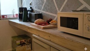 Een keuken met een magnetron, broodrooster en een snijplank met etenswaren.