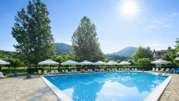 Una piscina rectangular con solárium de piedra, rodeada de sombrillas blancas y sillones de descanso.