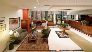 Un moderno vestíbulo de hotel con un sofá, una mesa de centro y sillones, un mostrador de recepción y grandes ventanales con vistas.