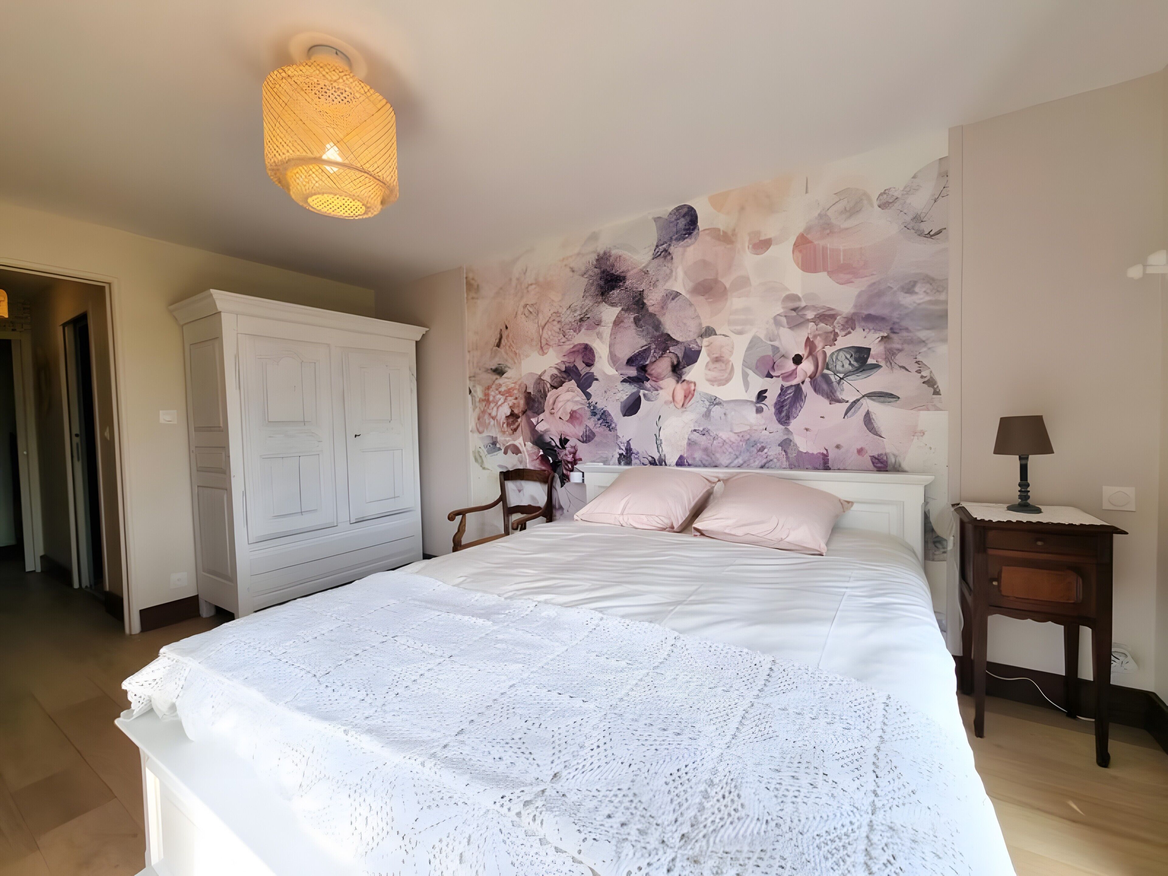 Een slaapkamer met een groot bed, een kledingkast, een stoel, een nachtkastje en een muur met een bloemenmural.