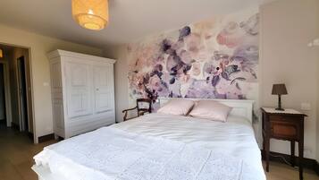 Een slaapkamer met een groot bed, een kledingkast, een stoel, een nachtkastje en een muur met een bloemenmural.