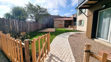 A residential property with a paved driveway, a wooden fence, a grassy lawn, and a brick patio area.