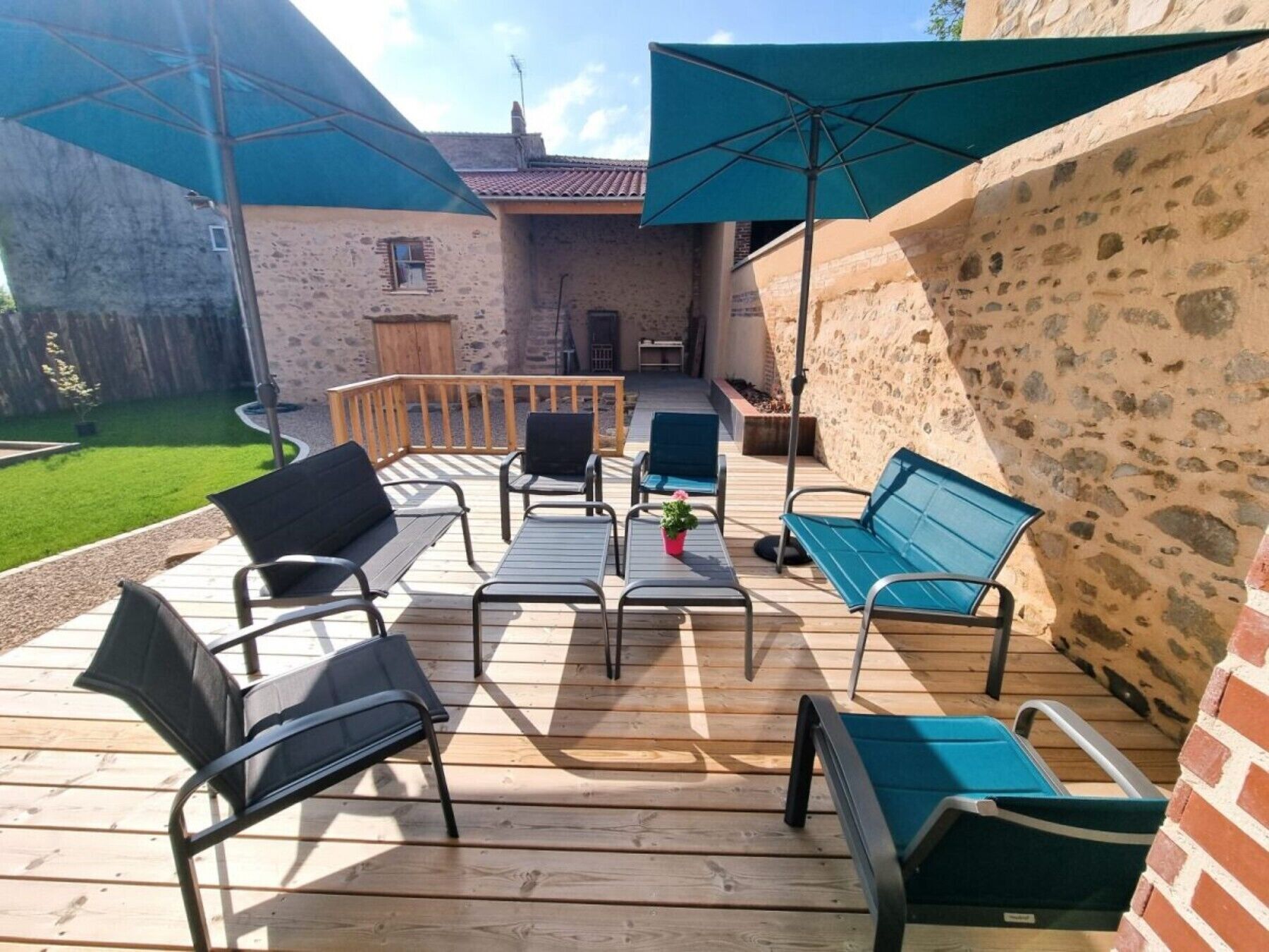Una terrazza esterna con pavimento in legno, sedie in metallo, una panca e una pianta in vaso.