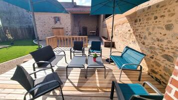 Una terrazza esterna con pavimento in legno, sedie in metallo, una panca e una pianta in vaso.