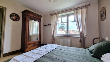 A bedroom with a bed, a dresser, a window with curtains, a radiator, and a wall clock.