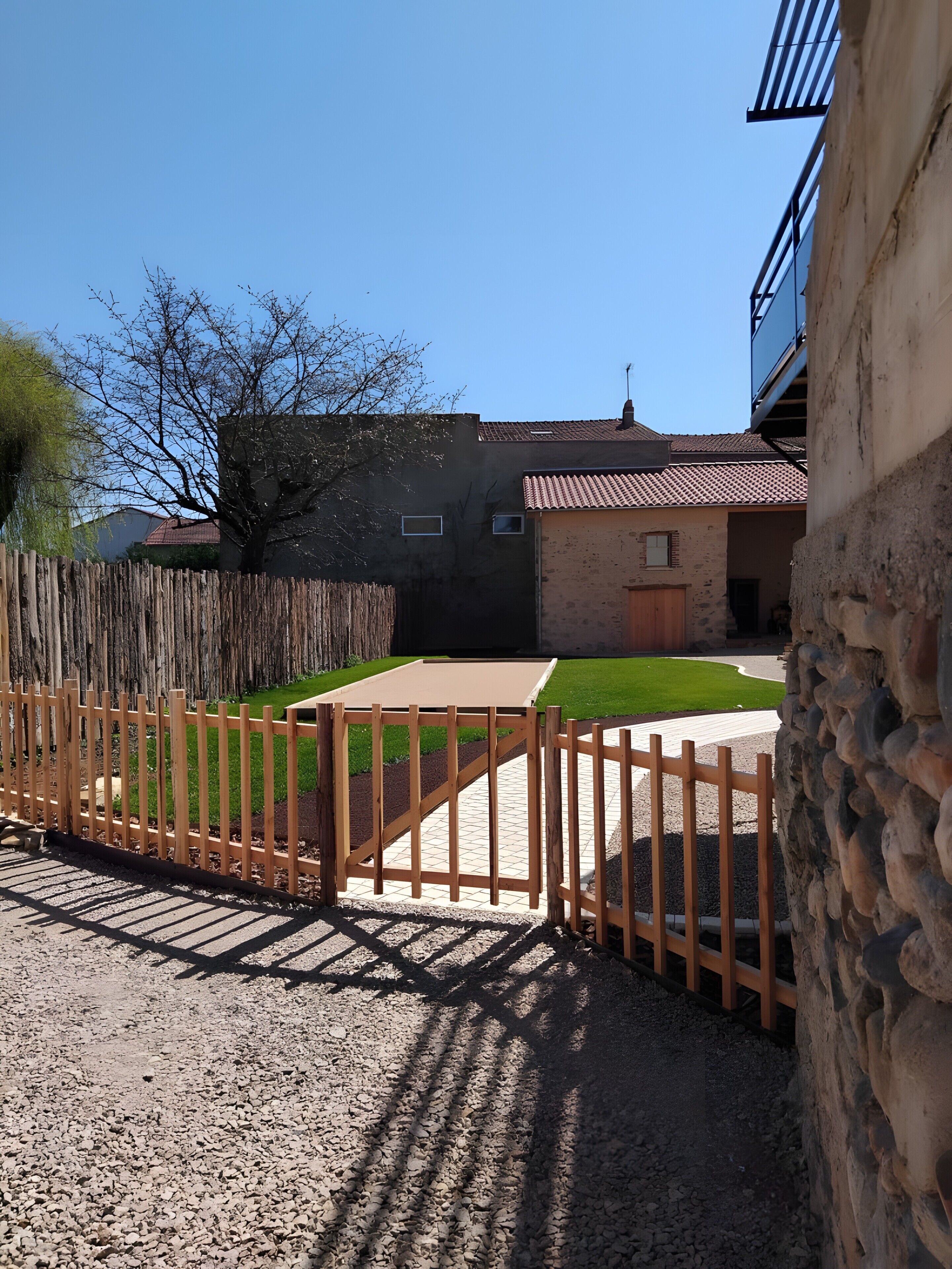 A residential area with a gravel driveway, a wooden fence, and a stone wall.