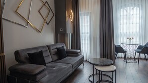 A modern living room with a grey sofa, a round coffee table, and a small side table. There is a window with sheer curtains and a view of the outside. - Nm Suites Beyoglu (Istanbul)