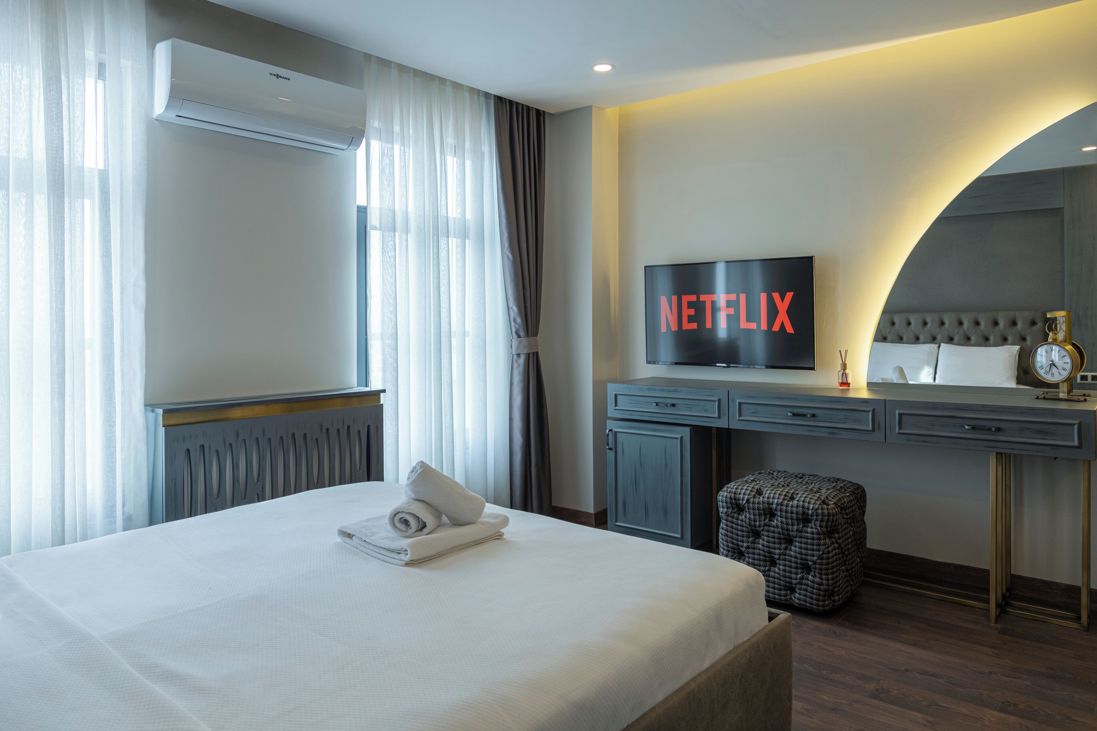 A hotel room with a bed, a desk, a television displaying "NETFLIX", and an air conditioning unit.