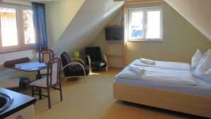 Una habitación pequeña y acogedora con cama, escritorio y silla. Hay una ventana que proporciona luz natural y vistas al exterior.