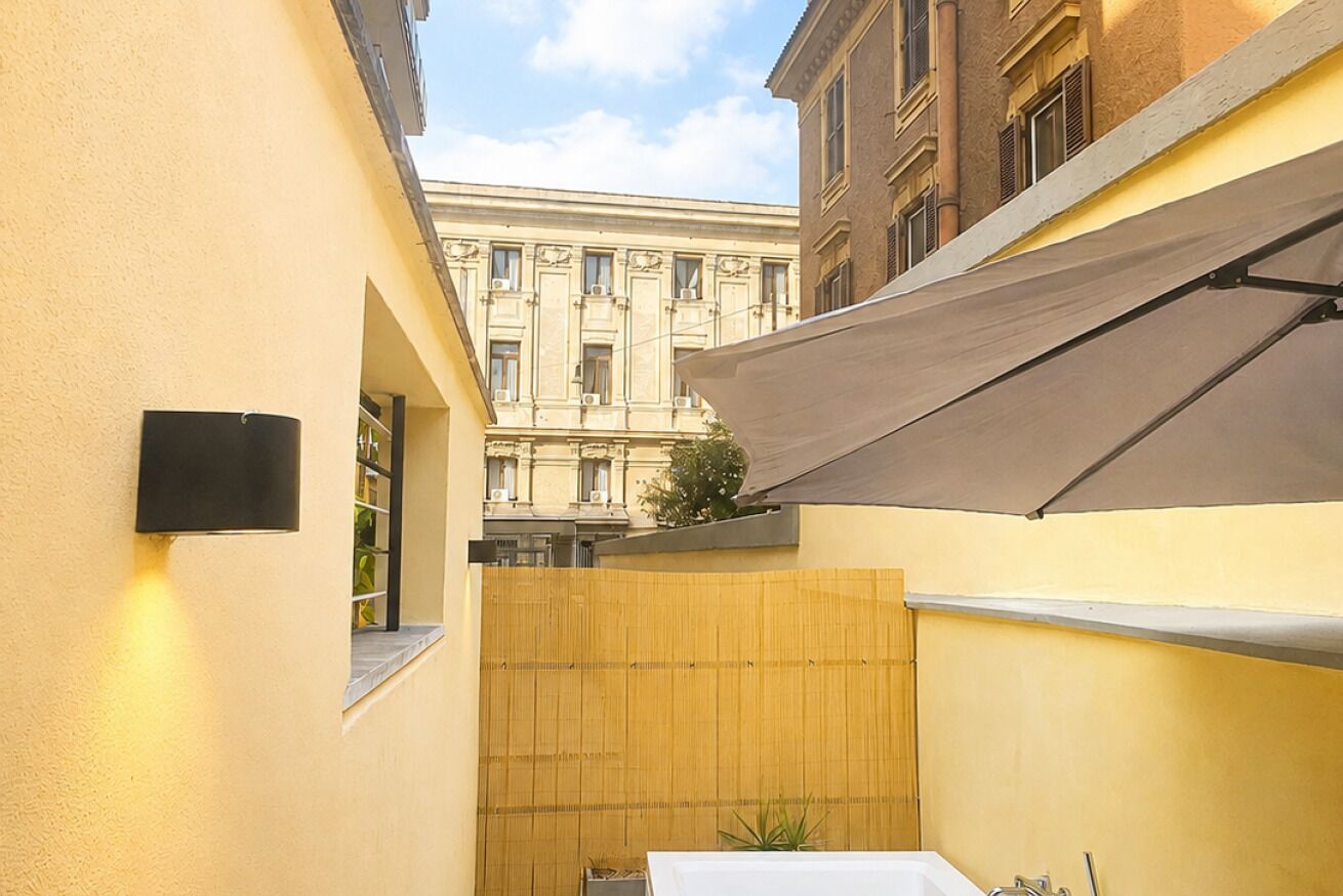 Une ruelle étroite, bordée d’une clôture en bois, avec une table blanche et, au fond, un bâtiment à l’architecture classique.