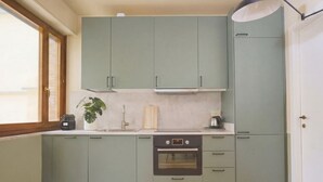 A kitchen with light green cabinets, a built-in oven, and a window providing natural light. - CS Trastevere Glorioso Signature Apt. (Rome)