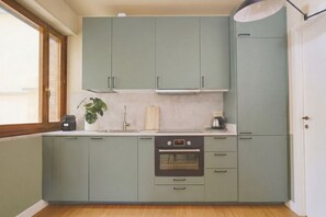 A kitchen with light green cabinets, a built-in oven, and a window providing natural light. - CS Trastevere Glorioso Signature Apt. (Rome)