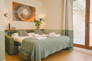 A bedroom with a bed, pillows, a green blanket, a potted plant, and a wall-mounted artwork. - CS Trastevere Glorioso Signature Apt. (Rome)