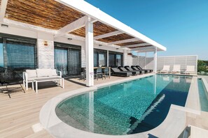 Un área de piscina moderna con sillones de descanso, una tumbona y una zona de estar cubierta.