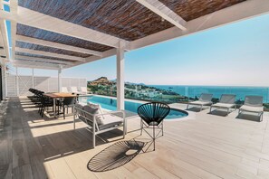 Un espacio al aire libre techado con piscina, sillones de descanso y una mesa.
