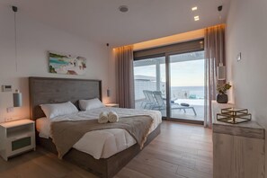 Una habitación de hotel moderna con una cama grande, vista al mar y un balcón con asientos.
