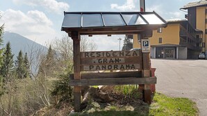 A wooden sign with 'RESIDENZA GRAN PANORAMA' written on it, a parking sign, and a building in the background. - Apartment 'Relax At The Mountain' with Mountain View, Shared Terrace and Wi-Fi (Madonna di Campiglio)