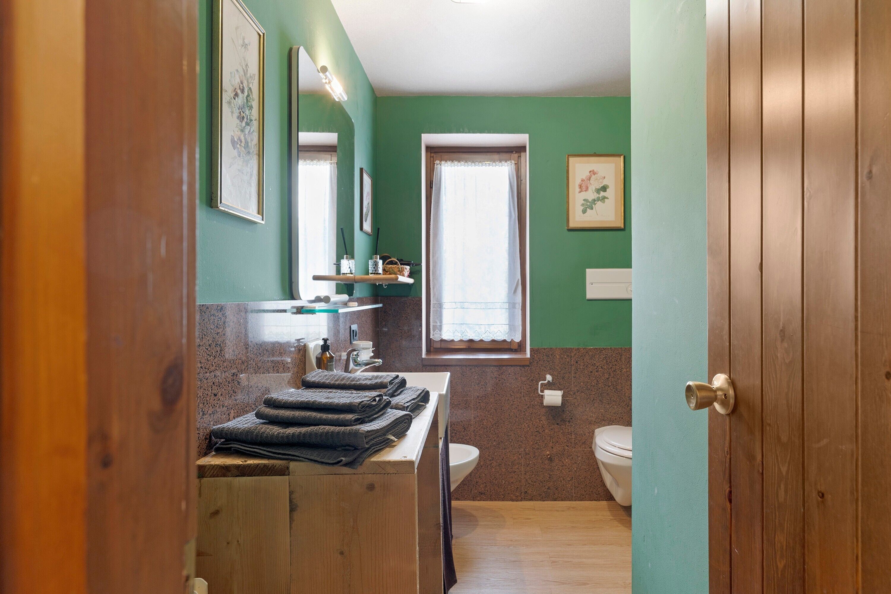 A bathroom with a wooden vanity, a sink, a toilet, and a window with a curtain.