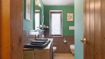 A bathroom with a wooden vanity, a sink, a toilet, and a window with a curtain.