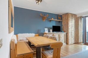 Et værelse med et træspisebord, en sofa, et fjernsyn og en vægmonteret hylde med dekorative genstande.