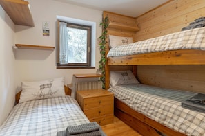 Et værelse med to køjesenge, en trækommode, et vindue med gardiner og en radiator.