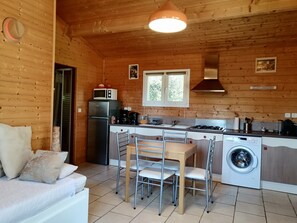 A wooden cabin interior with a kitchenette, a dining area with chairs, a washing machine, and a sofa with cushions.