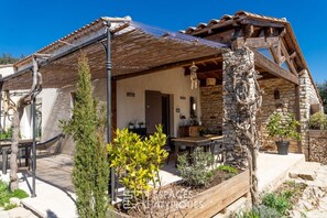 A rustic stone house with a wooden porch, a dining area, and a stone fireplace. - Guest Room “Toucan” with Private Terrace, Wi-Fi, and Air Conditioning (Gras)