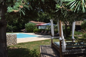 Un espace piscine avec des chaises longues, un coin salon abrité et un mur en pierre.