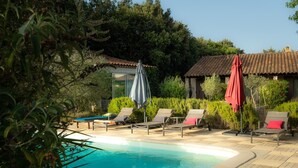 A pool area with lounge chairs and umbrellas, surrounded by greenery and a building with a tiled roof. - Unique 'Wapa Lodge' Accommodation with Shared Garden (Gras)