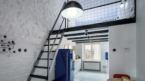 A kitchen with a blue refrigerator, a wooden table with yellow cups, and a staircase with a black railing. - RentPlanet - Apartament Lelewela (Wrocław)