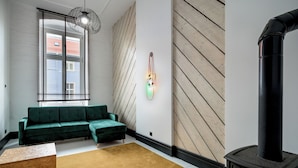 A modern living room with a green sofa, a wooden floor, a black fireplace, and a wall-mounted light fixture. - RentPlanet - Apartament Lelewela (Wrocław)