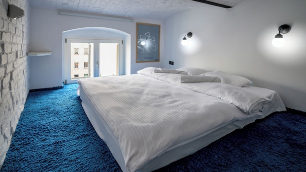 A bedroom with a large bed, a blue carpet, a white wall, and a door leading to a balcony. - RentPlanet - Apartament Lelewela (Wrocław)
