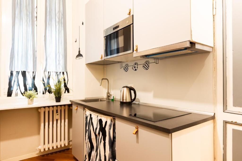A compact kitchen with a microwave, kettle, and a window with curtains.