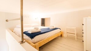 A single bed with a wooden frame, white bedding, and a blue throw blanket. A white step ladder is next to the bed, and a white wardrobe is in the corner.