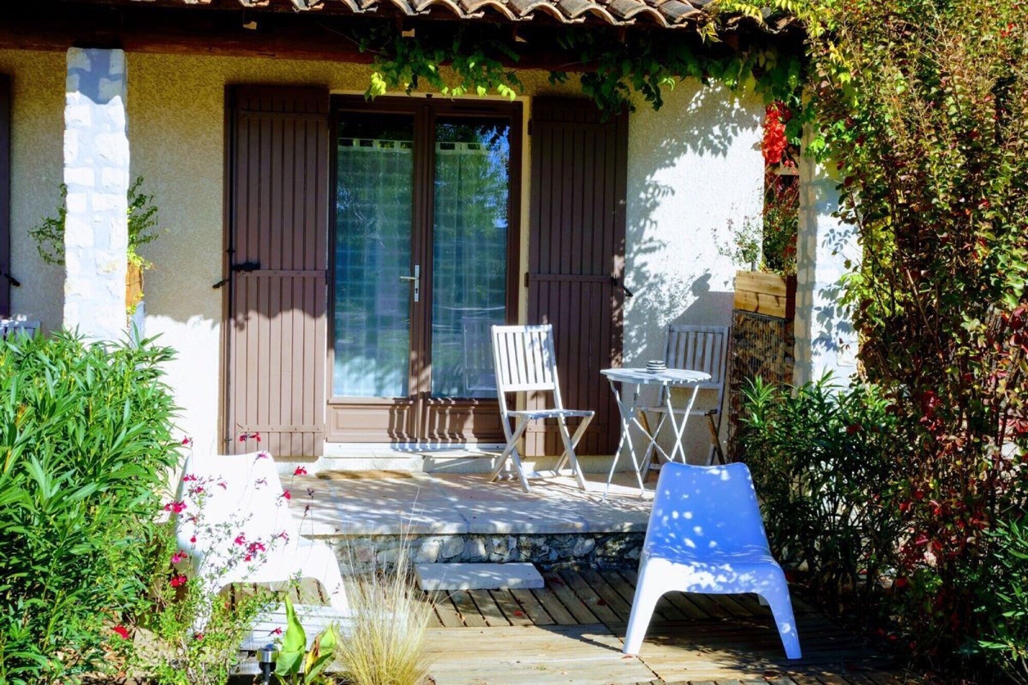 A covered outdoor seating area with a table and chairs, a small garden with plants, and a wooden deck.