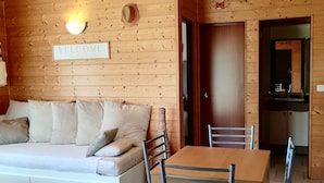 Un intérieur en bois comprenant un canapé, une table à manger, des chaises et une pancarte indiquant « BIENVENUE ».