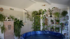Une pièce comprenant un grand bain à remous bleu, un meuble en bois orné de panneaux et un mur décoré de différents pots de plantes.