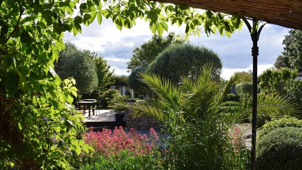Un jardin agrémenté d’une terrasse en bois, d’un mur en pierre et de diverses plantes et fleurs.
