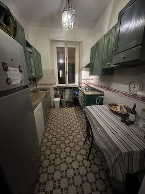 Una cocina funcional con piso de baldosas, un refrigerador, una estufa y armarios verdes.