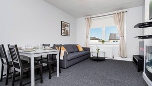 A compact living space with a dining area, a sofa, a TV, and a window with curtains. - Ideal Work Stays | 3BR | Free Parking | Sleeps 6 (Falkirk)