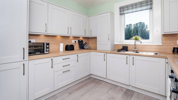 A modern kitchen with white cabinets, a wooden countertop, and a window with a view of trees. - Ideal Work Stays | 3BR | Free Parking | Sleeps 6 (Falkirk)